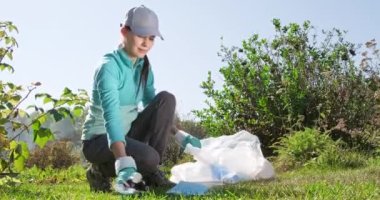 Çöp paketi taşıyan mutlu kız. Genç bir kadın gönüllü, çevre kampanyasına katılıyor ve parktaki plastik çöpleri temizliyor. ESG ve SDG kavramlarını kabul et