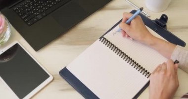 Üst manzara, kamera ahşap masanın üzerinde yavaşça hareket ediyor, hangi dizüstü bilgisayar, tablet, not defteri üzerine genç bir kadın not defterine yeni 2022 için planlar yazıyor. Noel ve yeni yıl konsepti