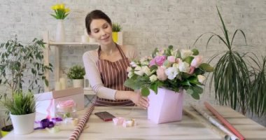 Genç bir çiçekçi kadın. İş kadını satışı ve çiçekçi konsepti. Çiçekçide gülümseyen bir kadın sürüyle para kazanıyor. Çiçekli güzel bir çiçekçi kız. Evde çalışan kadın çiçekçi.