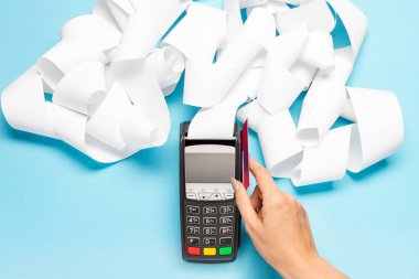 Mavi arka planda uzun kasiyer bandı olan pos terminal. Kadın eli kredi kartıyla öder. alışveriş teması