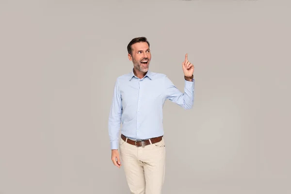 照片上是一位穿着浅蓝色衬衫 面带微笑的正式商人 站在灰色工作室的背景上指指点点 — 图库照片