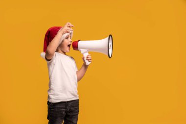 Noel Baba şapkalı, elinde megafonla gülümseyen ve çığlık atan komik çocuk stüdyo arka planında poz veriyor. Xmas konsepti. Bir sürü kopyalama alanı