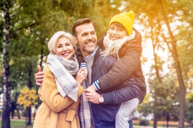 Gerçek insan yaşam tarzı ve aile duyguları kavramı. Mutlu anne, baba ve oğul birlikte eğleniyor, sonbahar parkında yürüyor.