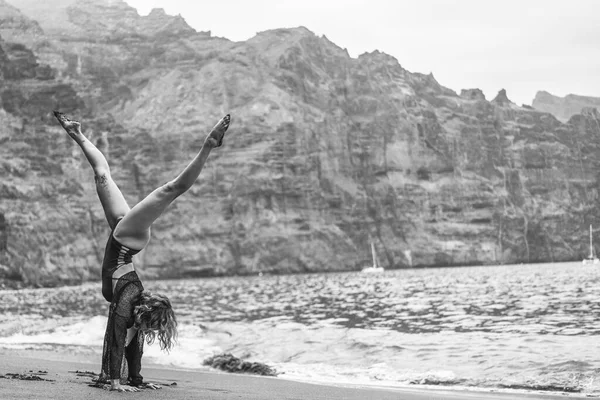 年轻的健身女子在岩石沙滩上做手倒立运动 在海滨练习瑜伽 早上例行公事Tenerife Los Gigantes — 图库照片