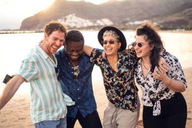 Bir grup mutlu çok ırklı arkadaş sahilde birlikte eğleniyor, dans ediyor ve gülüyorlar. Melez ırk arkadaşlığı kavramı. Çok ırklı öğrencilerin yaşam tarzı. Gerçek insanların duyguları.