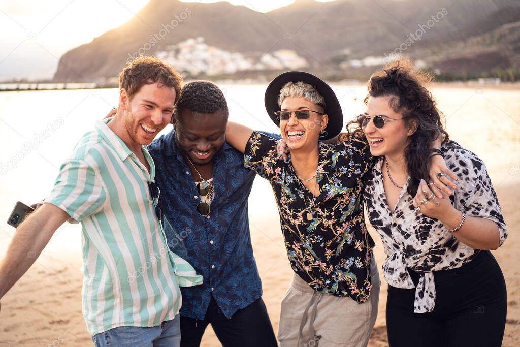 Group of happy multiracial friends having fun together on the beach, dancing and laughing. Mixed race people friendship concept. Multi ethnic students lifestyle. Real people emotions