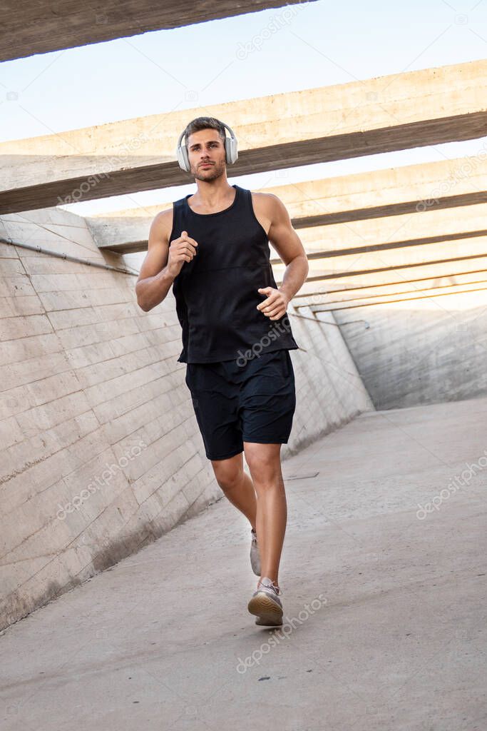 Sporty young man jogging with music from headphones, morning routine. Healthy lifestyle concept. Personal trainer.