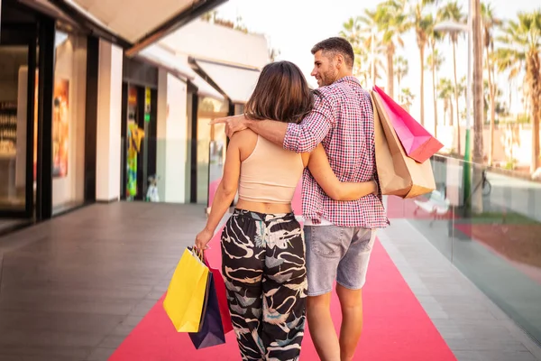 若いファッショナブルなカップルのショッピング バッグを手に歩いて笑顔 一緒に時間を過ごす リラックスして レジャー 消費主義の概念 バックビュー — ストック写真