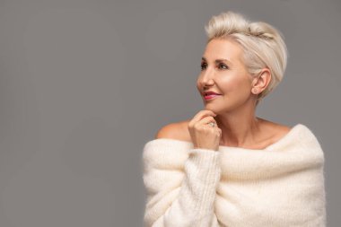 Beauty portrait of elegant adult blonde woman with short hairstyle and glamour makeup. Attractive lady wearing warm fashionable sweater. A lot of copy space. Studio shot.
