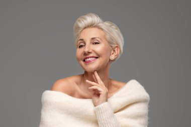 Kısa saç stili ve alımlı makyajlı gülümseyen sarışın bir kadının güzel portresi. Çekici bayan kalın, şık bir kazak giyiyor. Bir sürü kopya alanı var. Stüdyo çekimi.