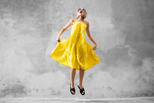 Happy Laughing Blonde Woman Jumping Yellow Dress Grey Wall Lot — стоковое фото