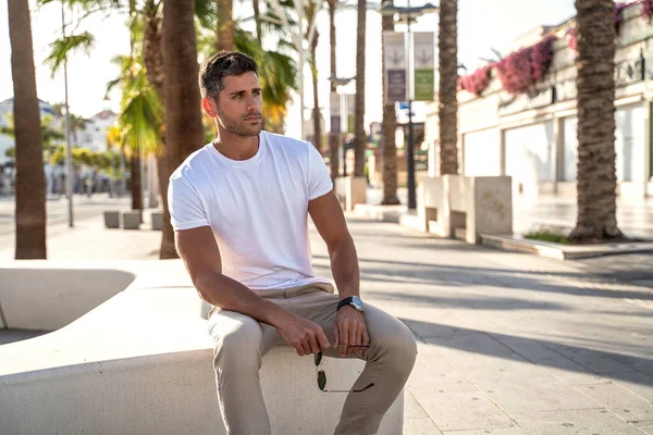 Şehrin arka planında poz veren beyaz tişörtlü yakışıklı bir genç. Sıradan bir tarz. Modaya uygun bir adam. Yaz titreşimleri.