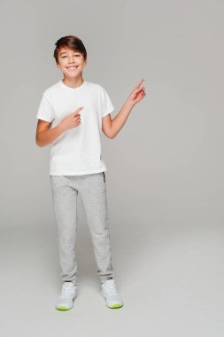 Happy smiling young boy in fashionable clothes pointing finger up over light grey studio background. A lot of copy space.   Education and school concept.