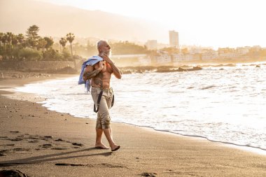 Sağlıklı bir bedende, sağlıklı bir zihinde. Gün batımında plajda yürüyen beyaz sakallı ve dövmeli son sınıf öğrencisi. Yaz tatili. Yaşlılar emeklilik kavramında sağlıklı bir yaşam tarzına sahipler