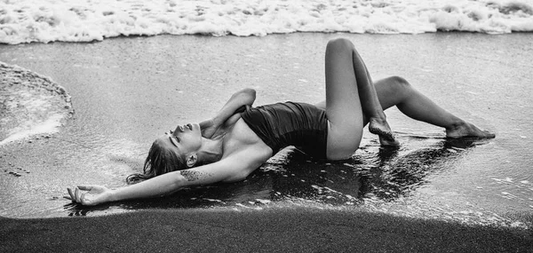 ファッショナブルな黒の水着で官能的な女性は 水の上に ビーチに横たわっていた 女の子とともにセクシー体 — ストック写真