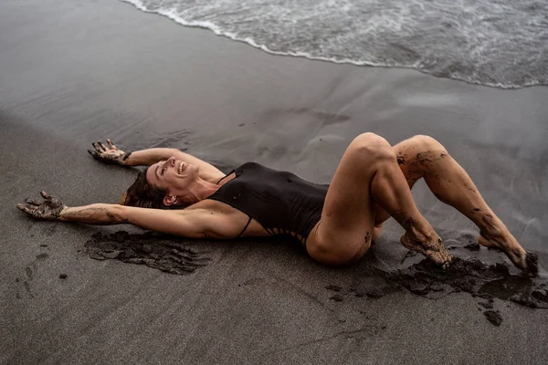 穿着时髦黑色泳衣的性感女人躺在黑色沙滩上 在海滩上 玩得很开心 夏天的感觉 — 图库照片