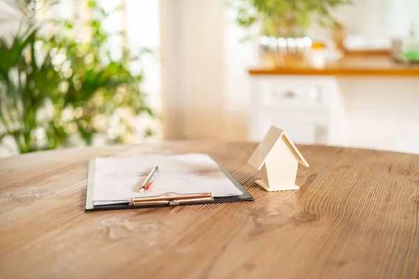 Wooden small model house and documents on the desk. Home insurance, investment, rental or purchase real estate and mortgages. House trading ideas.