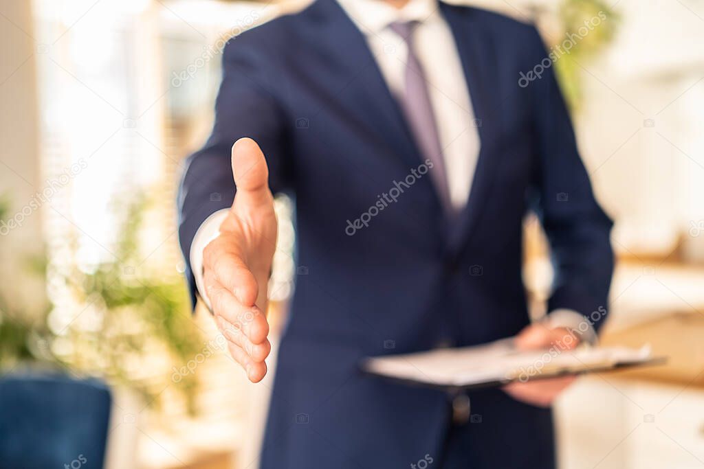 Conceptual photo of real estate or insurance agent with documents file. Man shakes the hand to the camera.