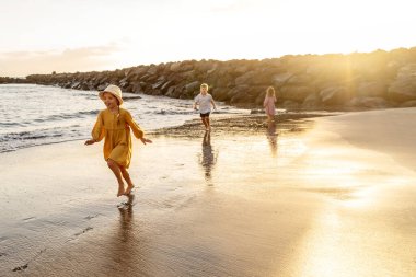 Kids playing on the beach. Little boy and girls running at sea shore at sunset. Family summer vacation vibes. A lot of copy space clipart