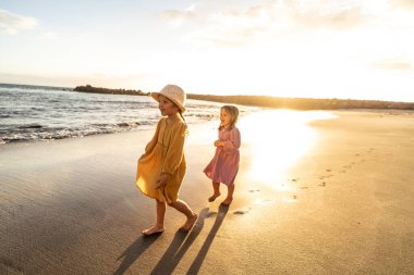 Kids playing on the beach. Little sisters walking at sea shore at sunset. Family summer vacation vibes. A lot of copy space clipart