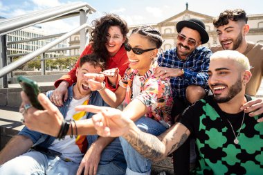 Çok ırklı öğrencilerden oluşan mutlu bir grup, dışarıda akıllı telefon kullanan arkadaşlar, sosyal medya izleyen, gülen, birlikte eğlenen. Modaya uygun insanlar selfie çekiyor.