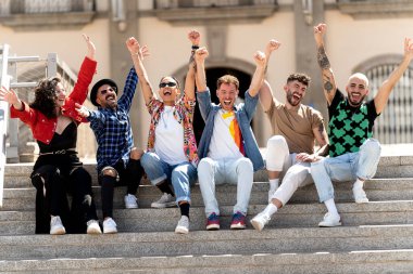 Çok ırklı bir grup mutlu genç arkadaş birlikte gülüyor ve üniversitenin yanında oturarak eğleniyorlar. Öğrenciler başarıyı kutluyor. Birlik ve toplum konsepti. Gerçek insanların duyguları ve yaşam tarzı.