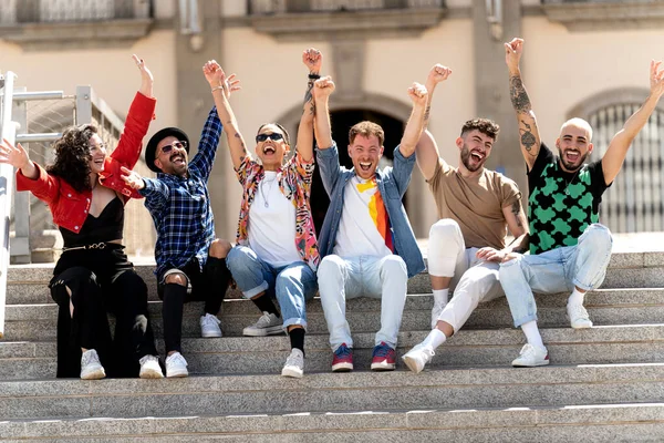 Çok ırklı bir grup mutlu genç arkadaş birlikte gülüyor ve üniversitenin yanında oturarak eğleniyorlar. Öğrenciler başarıyı kutluyor. Birlik ve toplum konsepti. Gerçek insanların duyguları ve yaşam tarzı.