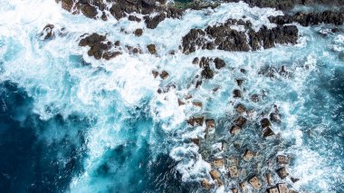 Büyük okyanus dalgalarının kayalık kıyıya çarpmasının en üst görüntüsü. Okyanusun gücü. Köpük spreyinin ve turkuaz deniz suyunun hava görüntüsü..