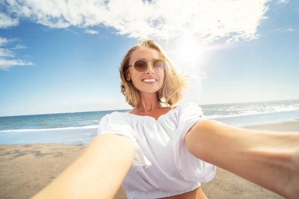 年轻美丽的金发女郎戴着太阳镜 在沙滩上自拍时对着相机微笑 女孩享受暑假的概念 游客人数 — 图库照片