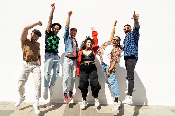 Bir grup mutlu genç arkadaş eğleniyor ve gülüyor, beyaz duvardan atlıyorlar. Çeşitli bin yıllık insanlar birlikte zaman geçiriyorlar. Arkadaşlık kavramı. Gerçek insan yaşam tarzı.