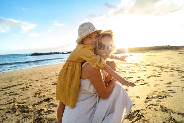 日落时 快乐的妈妈和她的小女儿一起在沙滩上玩乐 暑假期间 可爱的孩子与妈妈拥抱玩耍 真实的人的感情 家庭生活方式 — 图库照片