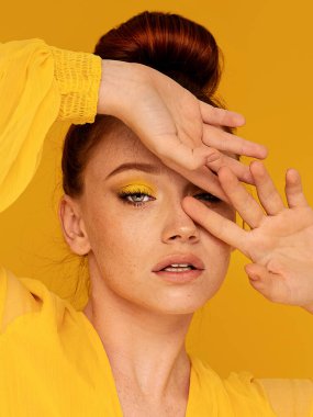 Sarı elbiseli güzel kızıl kadın kameraya bakıyor. Parlak kadın bakışı. Renkli bir arka plan ve makyaj. Bir sürü kopyalama alanı.