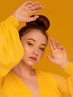 Sarı elbiseli güzel kızıl kadın kameraya bakıyor. Parlak kadın bakışı. Renkli bir arka plan ve makyaj. Bir sürü kopyalama alanı.