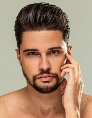 Yakışıklı sakallı esmer adam üstsüz poz veriyor, kameraya bakıyor. Erkek güzelliği, cilt konsepti. Bir sürü kopyalama alanı.
