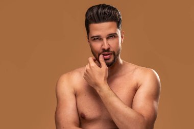 Seksi sakallı esmer adam üstsüz poz veriyor, kameraya bakıyor. Erkek güzelliği, cilt konsepti. Bir sürü kopyalama alanı. 