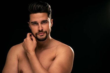 Beauty portrait of handsome, sexy male model with beard looking at the camera. Shirtless man posing on the black studio background. 