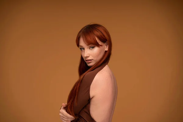 Ginger beauty girl with natural freckles, long healthy hair and fringe. Attractive red head woman posing in studio, looking at the camera. A lot of copy space