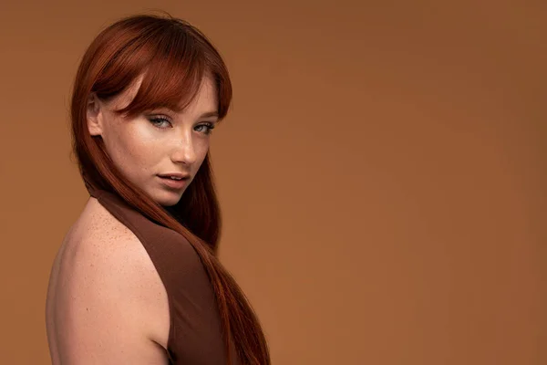 Ginger beauty girl with natural freckles, long healthy hair and fringe. Attractive red head woman posing in studio, looking at the camera. A lot of copy space