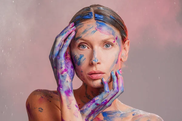 Beauty art portrait of a female painter with colorful paints on hands and face. Woman with blue eyes.
