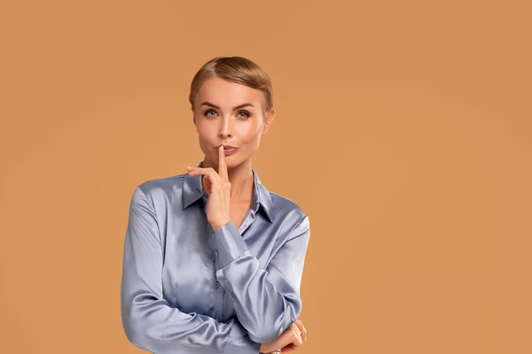 Beauty blonde woman with short hairstyle holding finger at lips, showing silence sign. Attractive young woman saying shh. A lot of copy space on studio background.
