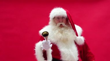Mutlu Noel Baba kırmızı stüdyo arka planında altın bir çan çalıyor. Xmas zamanı. Noel titreşimleri.