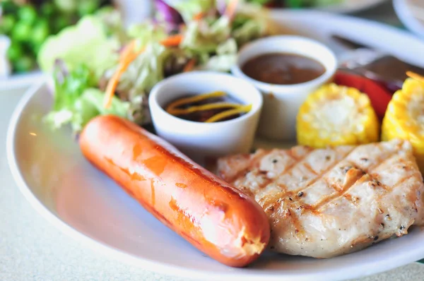 Steak de porc à la saucisse et salade de légumes sur plat blanc — Photo