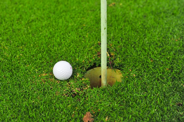 Uma bola de golfe branca perto do buraco — Fotografia de Stock