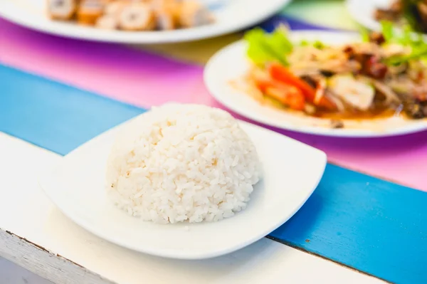 Rice in a white disc on colorful wood table — Stock Photo, Image