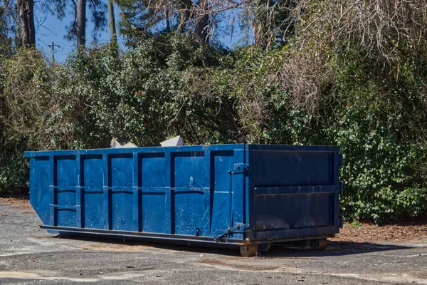 A blue open top dumpster filled with waste on a vacant lot in Georgia