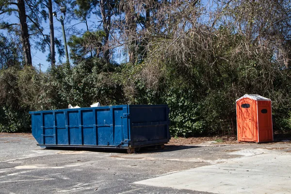 Orange porta potty and blue open top dumpster on a vacant lot