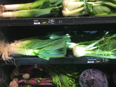 Marketteki raflarda bir demet pırasa ve kırmızı lahana.