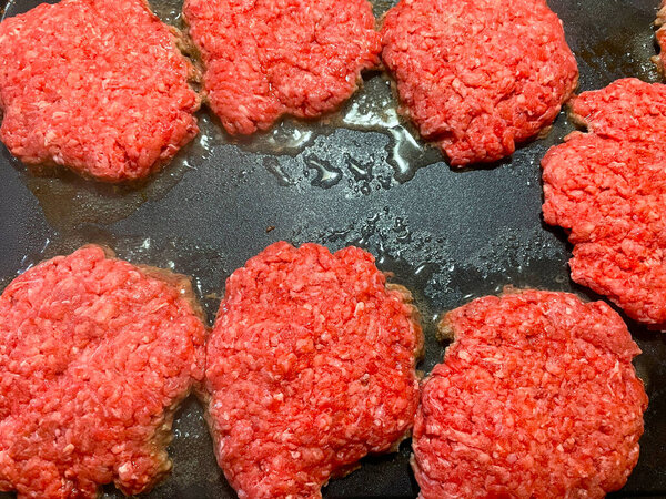 Raw hamburger meat patties frying on a griddle table top fryer
