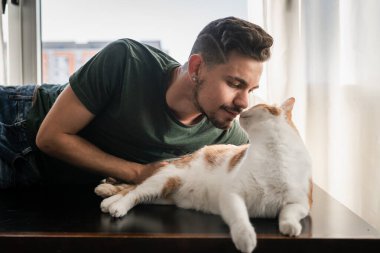 Genç adam ve kahverengi kedi birbirlerine bakıyorlar. Kapat.