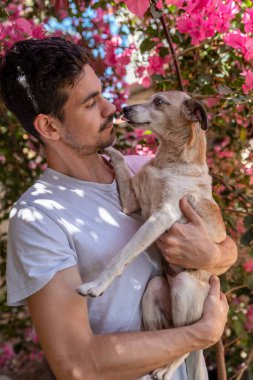 Genç adam kollarında bahçede bir köpek tutuyor. dikey bileşim